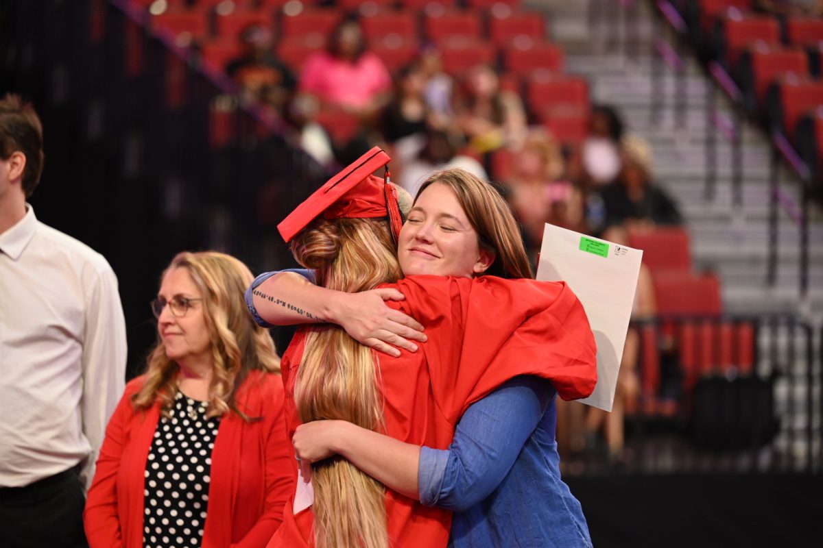 English teacher Marisa Zornes offers a celebratory hug to a new graduate at Saturday's Commencement as Business teacher Kim Pickering looks on.