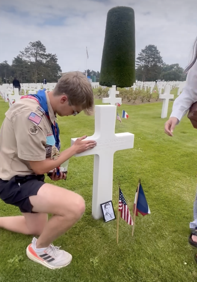 Chris Dickson (LHS '24) rubs dirt brought from Lincoln High School into the burial marker at the Normandy American Cemetery at the 80th anniversary of D-Day on Thursday.