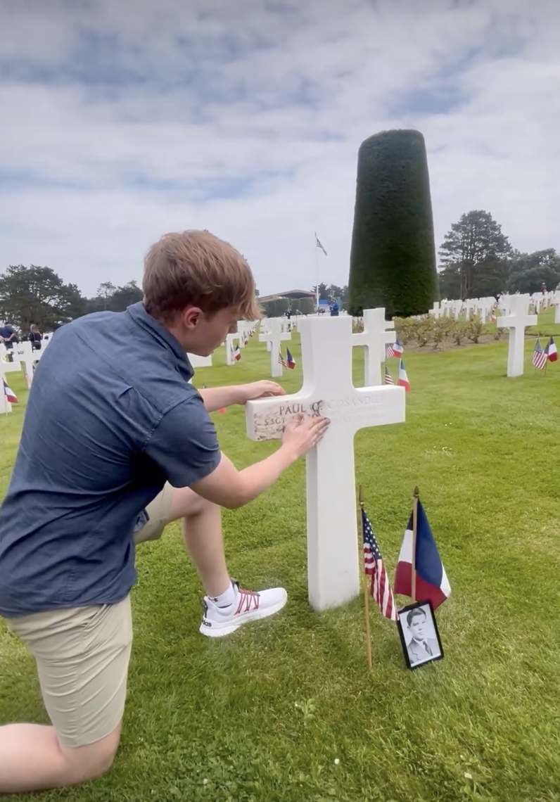 Garret Carter (LHS '24) rubs dirt brought from Lincoln High School into the burial marker at the Normandy American Cemetery at the 80th anniversary of D-Day on Thursday.