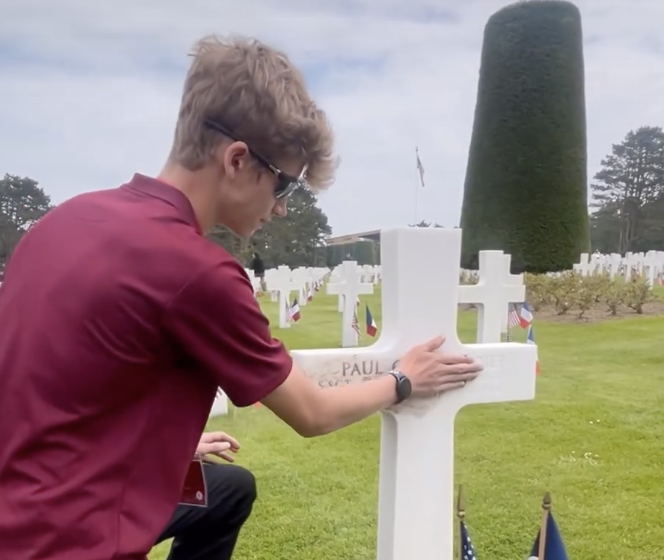 Sean Butler (10) rubs dirt brought from Lincoln High School into the burial marker at the Normandy American Cemetery at the 80th anniversary of D-Day on Thursday.